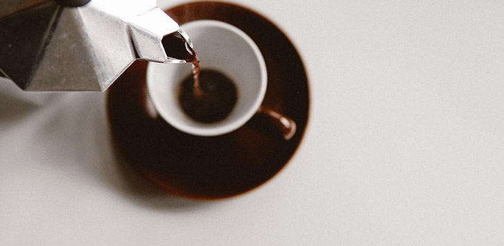 Pouring coffee from a moka pot into an white espresso cup