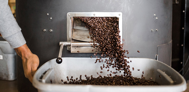 Roasted coffee beans pour out of the roaster into a container
