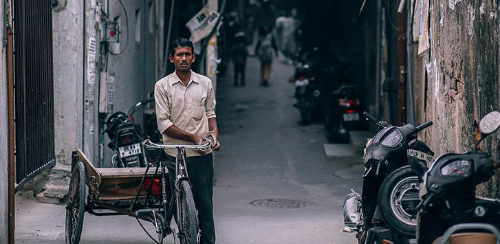 A man walks next to his bicycle in the streets