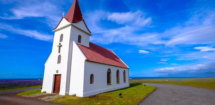 A white church surrounded by bright blue sky and lush green land